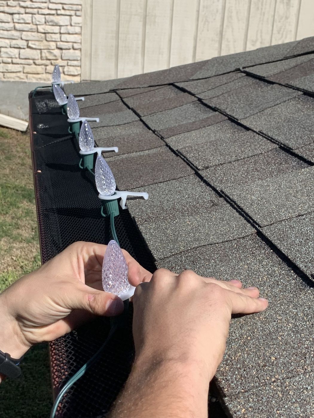Hand clipping a C9 Christmas light bulb onto a gutter with a professional clip