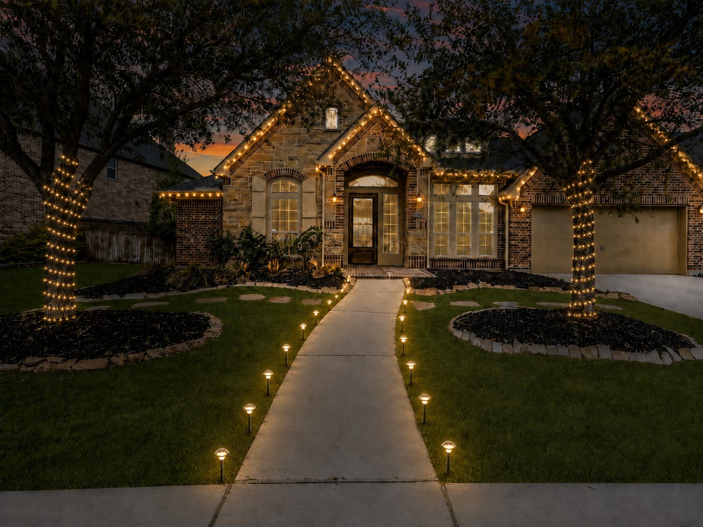 Texas Hill Country home with warm white roofline Christmas lights, wrapped oak trees and lit walkway at dusk